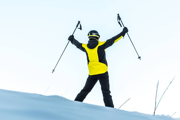 back view of skier in helmet holding sticks while standing on white snow 