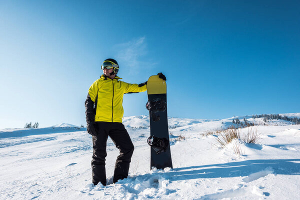 sportsman in helmet holding snowboard while standing on white snow 