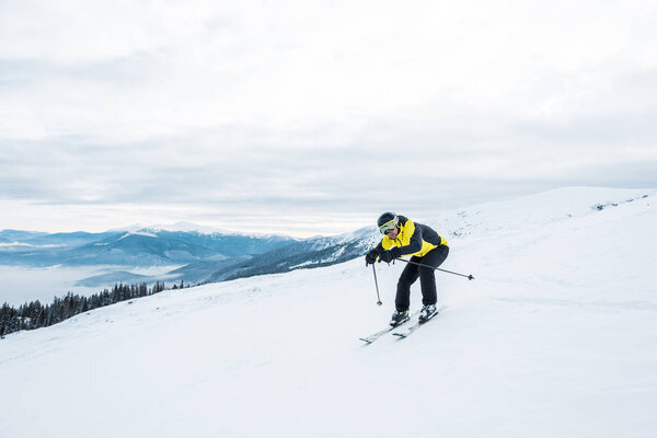 sportsman holding ski sticks and skiing on white slope in mountains 