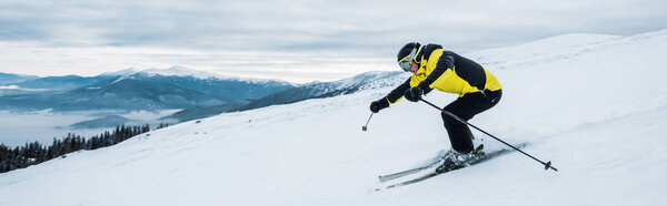 panoramic shot of sportsman skiing on slope in mountains 