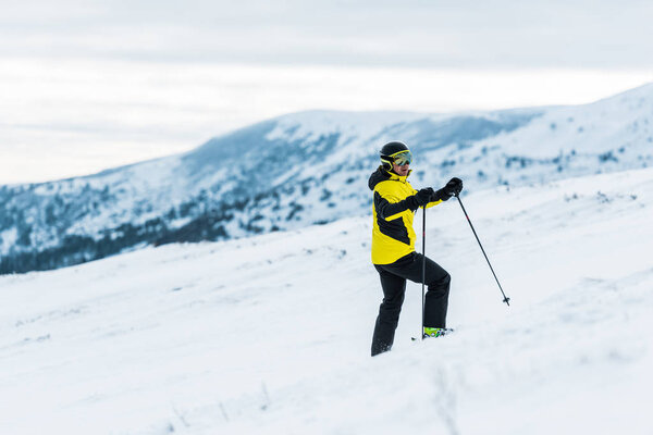 skier in helmet holding sticks and standing on slope in wintertime 