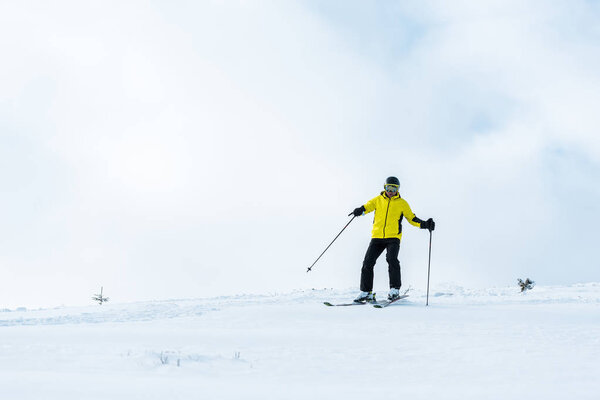 sportsman in helmet holding sticks and skiing on slope with snow in mountains 