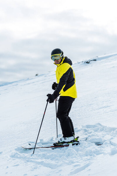 skier in helmet holding sticks and standing on slope outside 