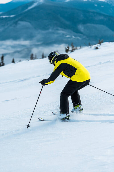 skier in helmet holding sticks and skiing on slope near mountains 