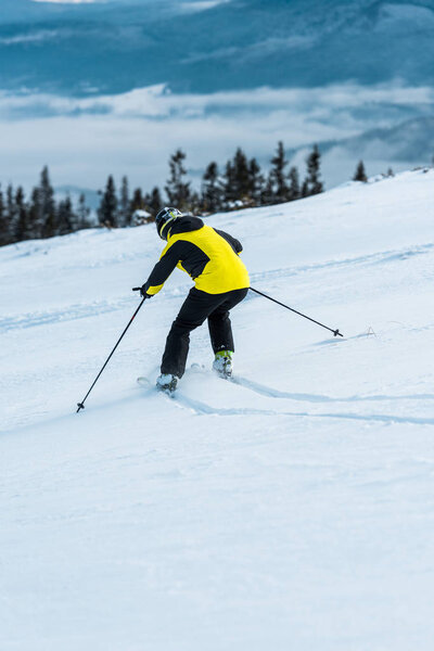 back view of skier in helmet skiing on slope near mountains 