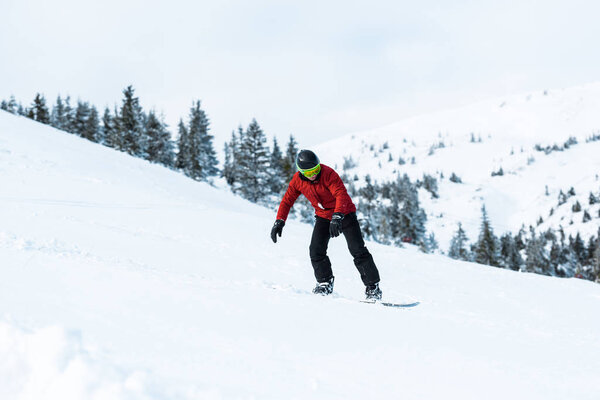 athletic snowboarder in helmet riding on slope in mountains 