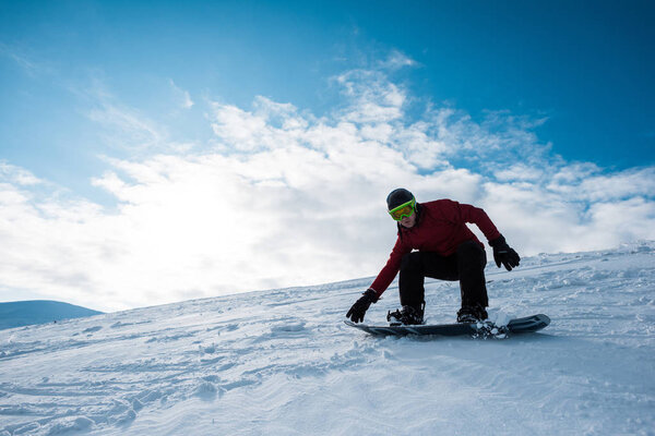 athletic snowboarder in helmet riding on slope against blue sky 