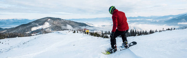 panoramic shot of snowboarder in helmet riding on slope in wintertime 