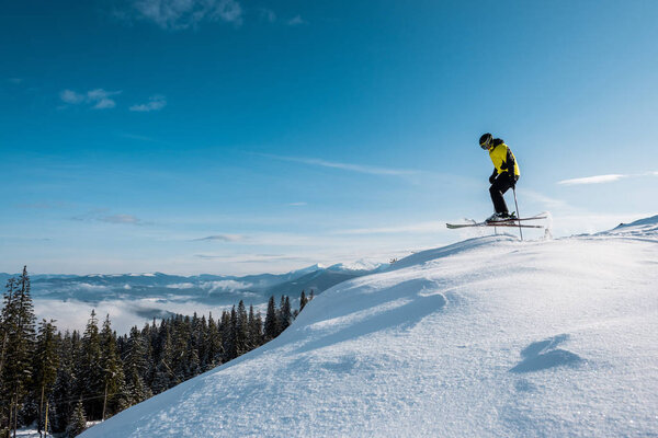 side view of skier holding ski sticks and jumping against blue sky in mountains 