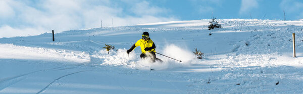 panoramic shot of skier in helmet holding ski sticks while skiing on slope outside 