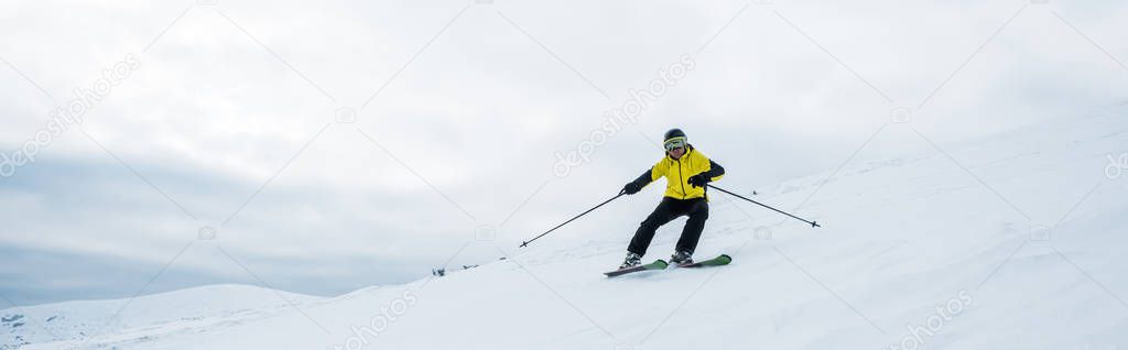 panoramic shot of sportsman holding ski sticks while skiing on white snow 