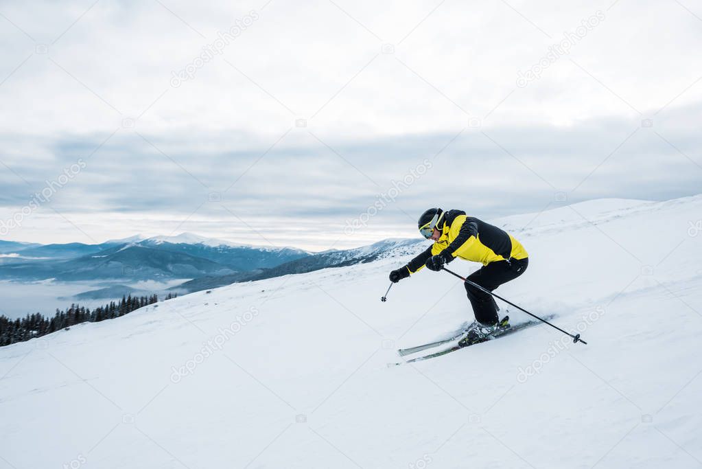 athletic man in helmet and goggles skiing on slope  