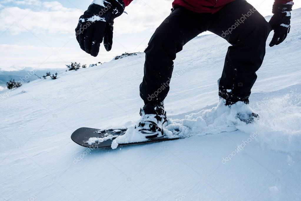 cropped view of snowboarder in gloves riding on slope with white snow in wintertime 