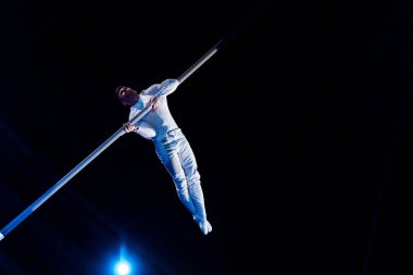 low angle view of man balancing while holding metallic pole in arena of circus  clipart