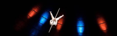 panoramic shot of acrobat balancing on pole in arena of circus  clipart