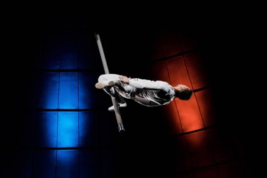 Sirkte mavi ve kırmızı ışıkta metalik kutupta dengede duran atletik akrobat 