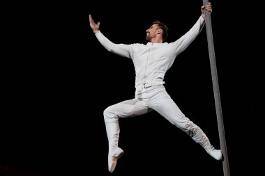 strong acrobat posing while performing and holding metallic pole isolated on black  clipart
