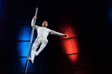 strong acrobat holding metallic pole while performing in circus  clipart
