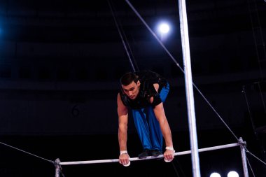 handsome gymnast performing on horizontal bars in arena of circus   clipart