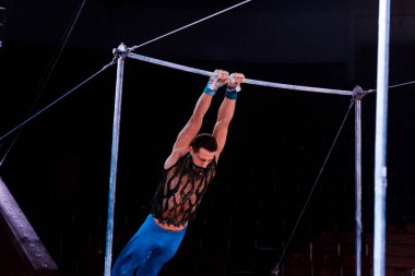athletic man performing on horizontal bars in arena of circus   clipart