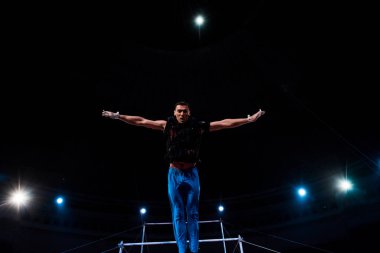 Sirk arenasında yatay barların yanında uzanan elleri olan atletik jimnastikçi  