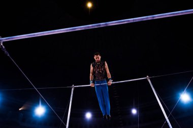low angle view of athletic gymnast performing on horizontal bars in arena of circus   clipart