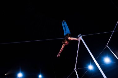 Düşük açılı atletik adam sirk arenasında yatay barlarda performans sergiliyor  