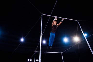 Esnek jimnastikçi sirk arenasında yatay barlarda gösteri yapıyor.  