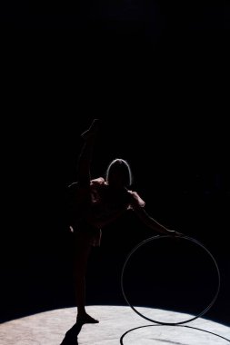 silhouette of flexible acrobat standing with hula hoop in arena of circus  clipart