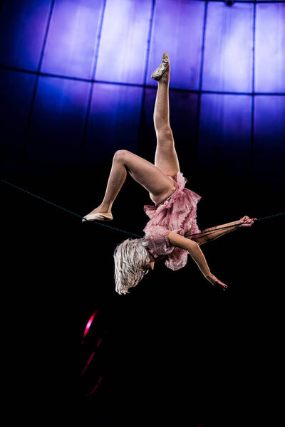 attractive aerial acrobat performing in circus near blue light 