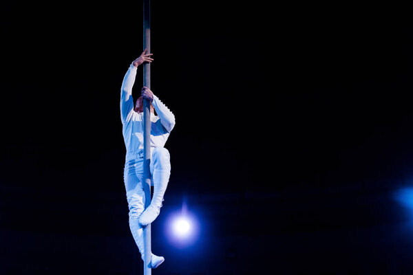 acrobat balancing while holding metallic pole in arena of circus 