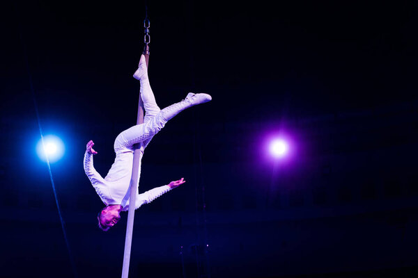 acrobat balancing on metallic pole in arena of circus 