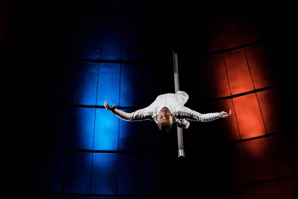 strong acrobat with outstretched hands performing on metallic pole 