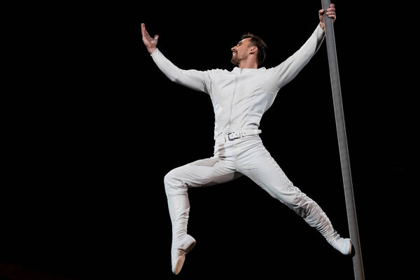 strong acrobat posing while performing and holding metallic pole isolated on black 