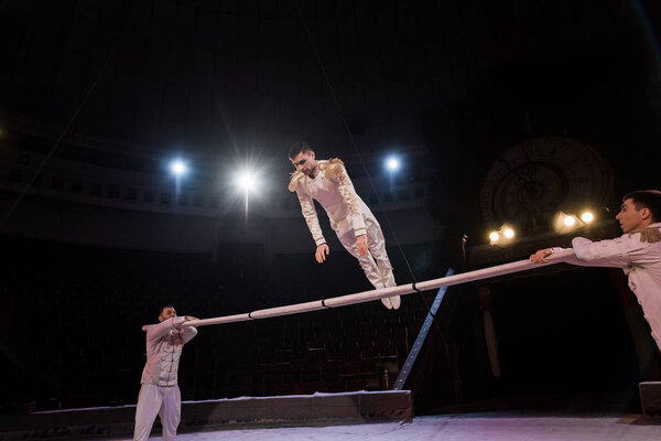 handsome gymnast exercising on pole near acrobats in circus