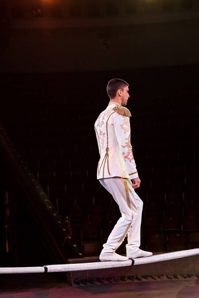 side view of handsome gymnast standing on pole in arena of circus 