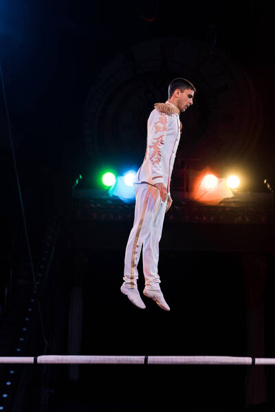 handsome gymnast balancing near pole in arena of circus 