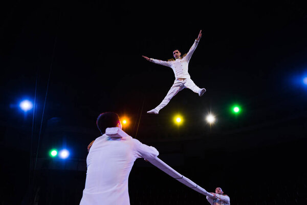 low angle view of handsome air acrobat with outstretched hands jumping near pole in arena of circus 