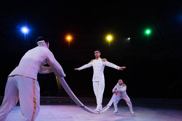 selective focus of handsome air acrobat balancing on pole near men in circus 