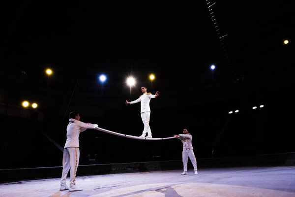 flexible air acrobat balancing on pole near men in circus 