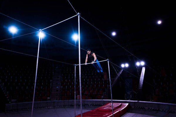 handsome gymnast performing on horizontal bars in circus  