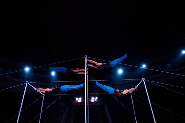 four acrobats performing on horizontal bars in circus  