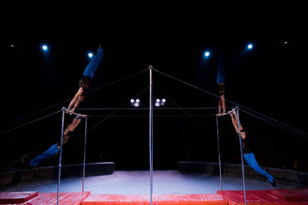 four gymnasts performing on horizontal bars in arena of circus  
