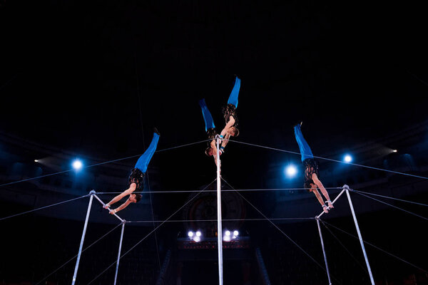 low angle view gymnasts performing on horizontal bars in arena of circus  