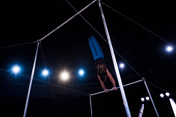 back view gymnast performing on horizontal bars in circus  