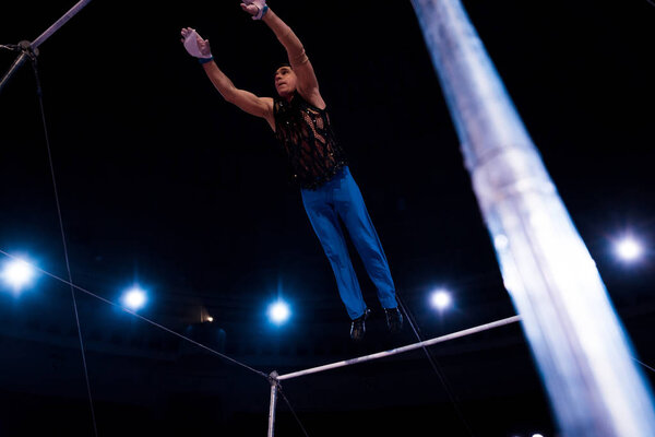 selective focus of handsome gymnast performing on horizontal bars in circus  