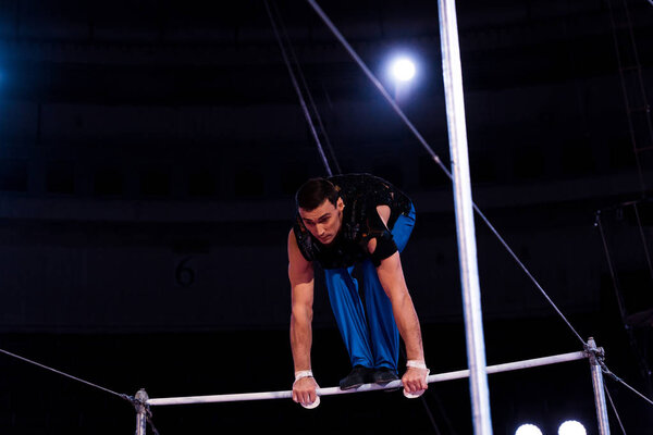 handsome gymnast performing on horizontal bars in arena of circus  