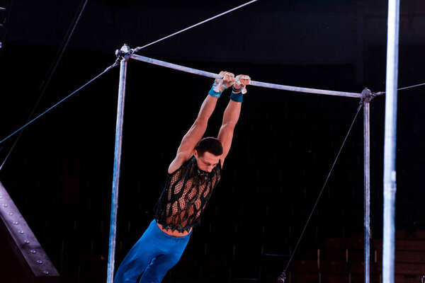 athletic man performing on horizontal bars in arena of circus  