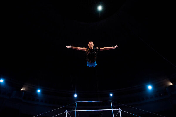 athletic gymnast with outstretched hands in arena of circus  