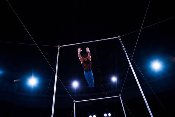 athletic gymnast jumping while performing on horizontal bars in arena of circus  